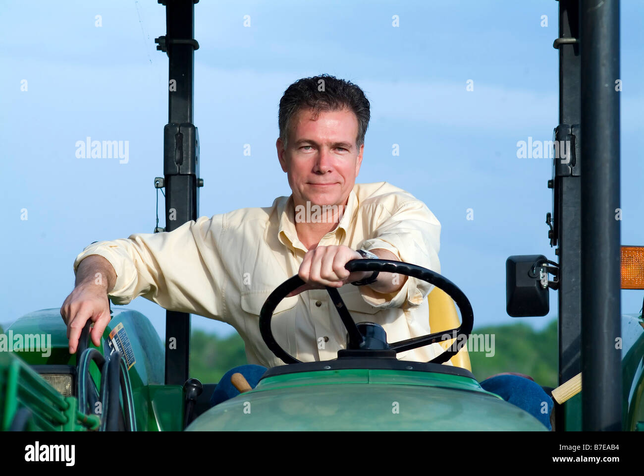 Schöne Reife weißer Mann sitzen bequem auf einem großen grünen Traktor lächelte zufrieden und selbstbewusst Stockfoto