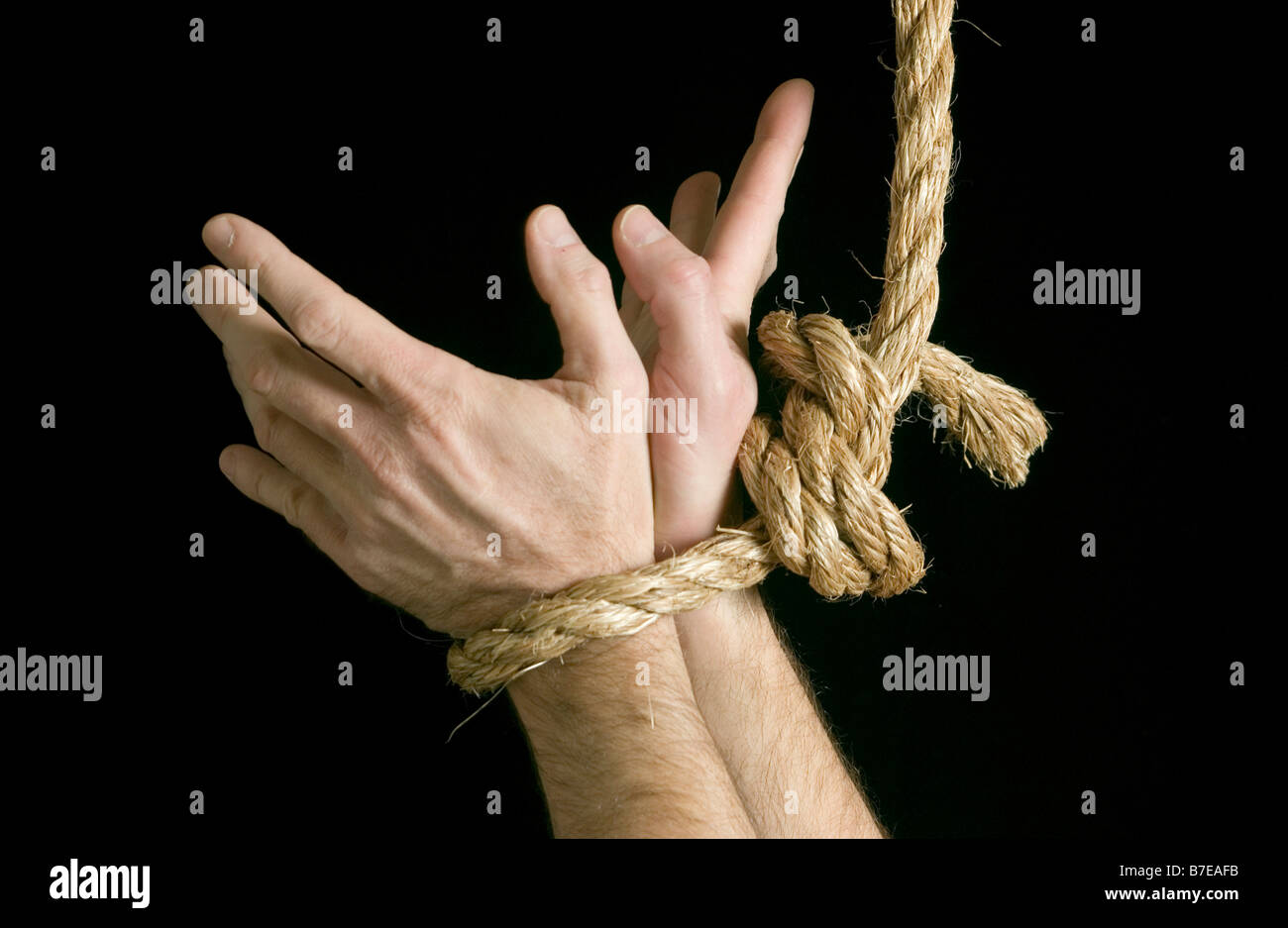 Hände eines kaukasischen männlichen gebunden zusammen mit einem langen Seil mit Fingern Ausbreitung breit als ob kämpfen, um sich zu befreien Stockfoto