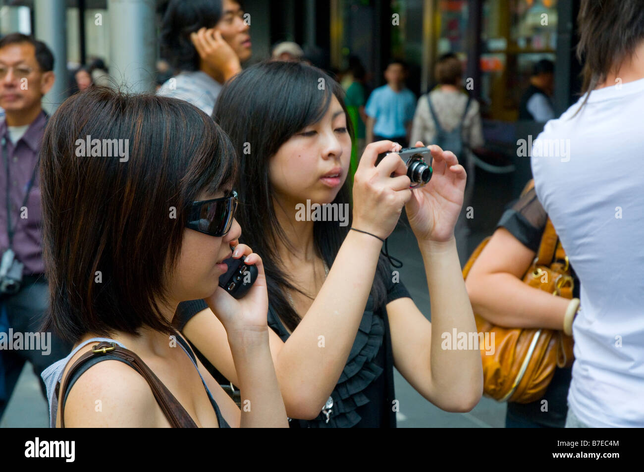 Zwei junge asiatische Mädchen mit Hilfe moderner Technologie in Form von einem Mobiltelefon und einer Digitalkamera Stockfoto