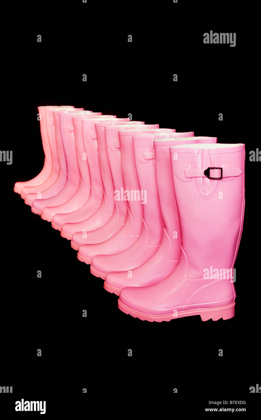 6 Paar rosa Gummistiefel oder Gummistiefel diagonal hintereinander vor schwarzem Hintergrund Stockfoto