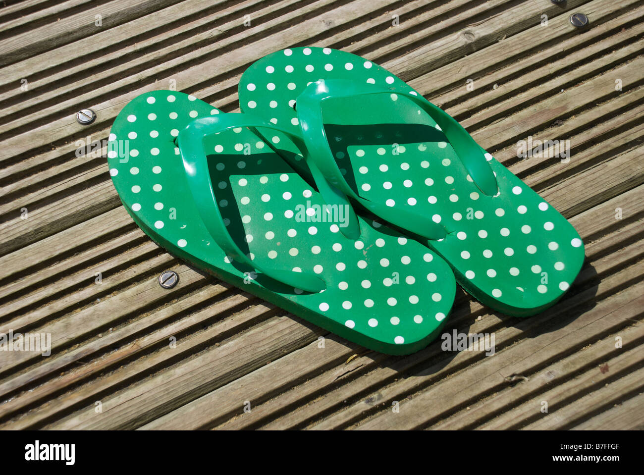grün weiss Poka Dot Flip-Flops Flecken decking Deck Sommer Holz Sonne Gummi-Füße Zehen Stockfoto