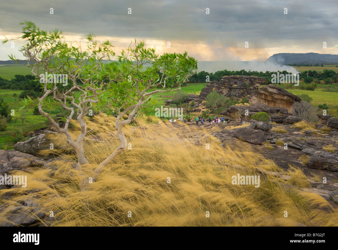 Touristen sitzen auf den Felsen des Ubirr mit einem Feuer im Hintergrund im Kakadu National Park Stockfoto