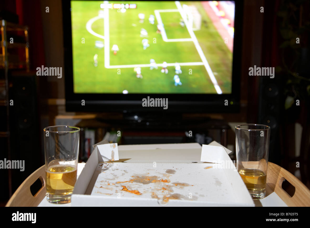eine Pizza zum Mitnehmen-Mahlzeit für zwei Personen und Gläser Bier auf einem Tablett vor Fußballspiel auf dem tv im Wohnzimmer des Hauses bleibt Stockfoto