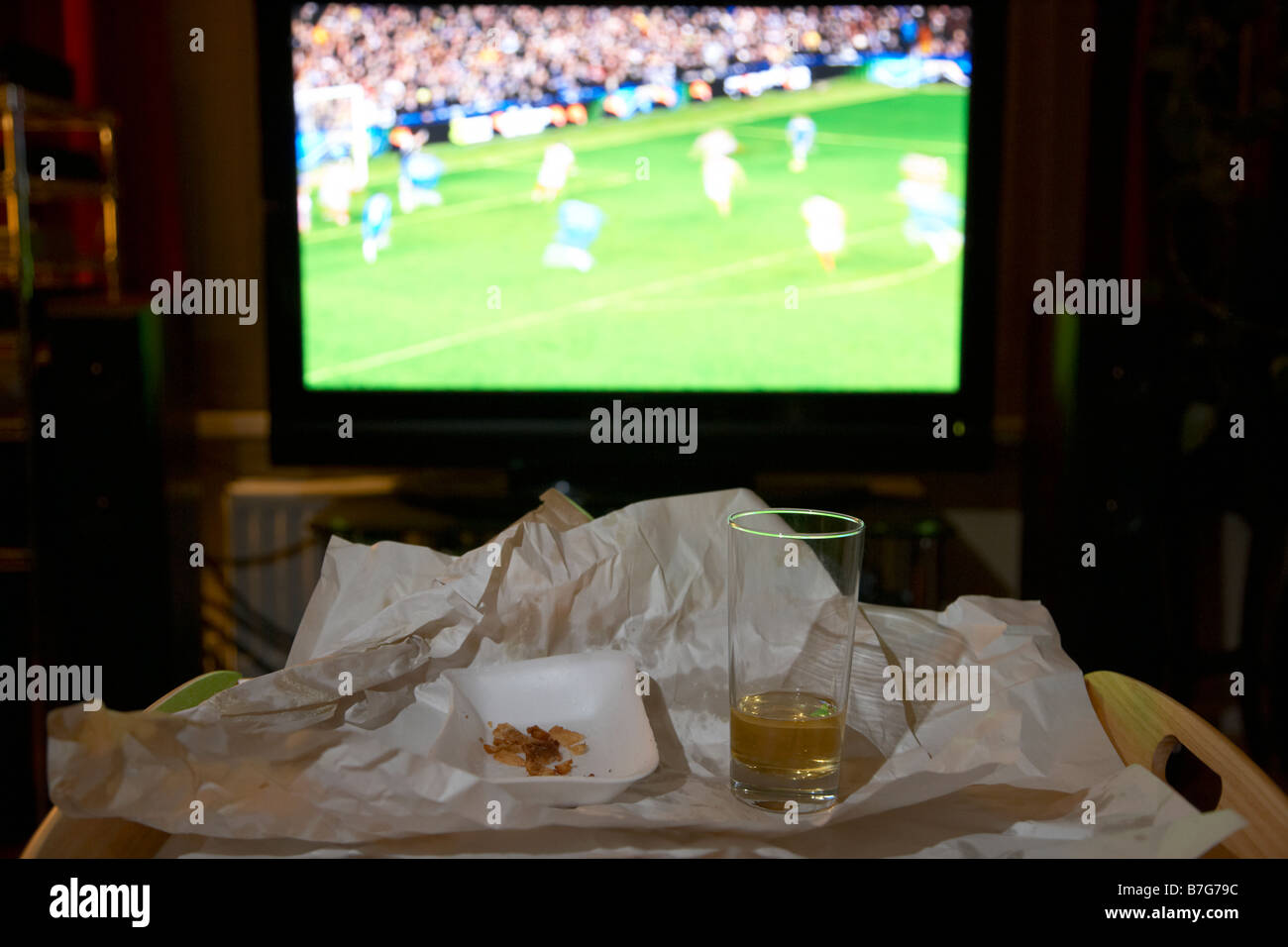 bleibt eine Mahlzeit zum Mitnehmen für eine und Glas Bier auf einem Tablett vor Fußballspiel auf dem tv im Wohnzimmer eines Hauses Stockfoto