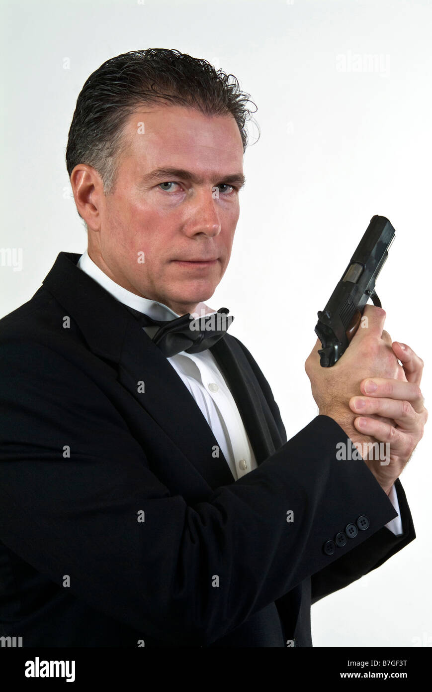 Ein Mann in formelle Kleidung hält eine automatische Pistole gegen einen weißen Hintergrund Stockfoto