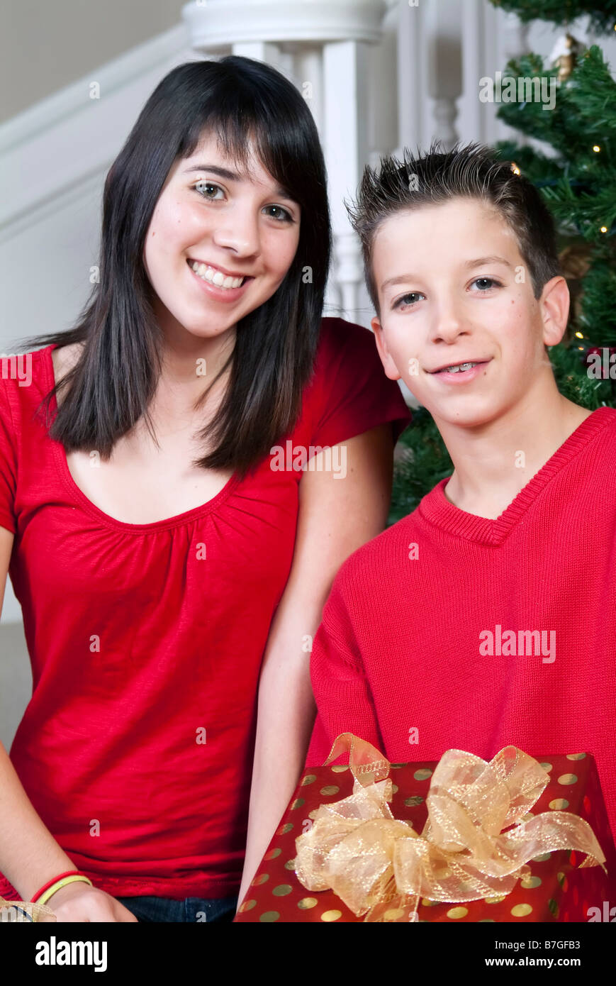 Bruder und Schwester von einem Weihnachtsbaum hält ein Geschenk mit schönen lächelnden Gesichtern Stockfoto