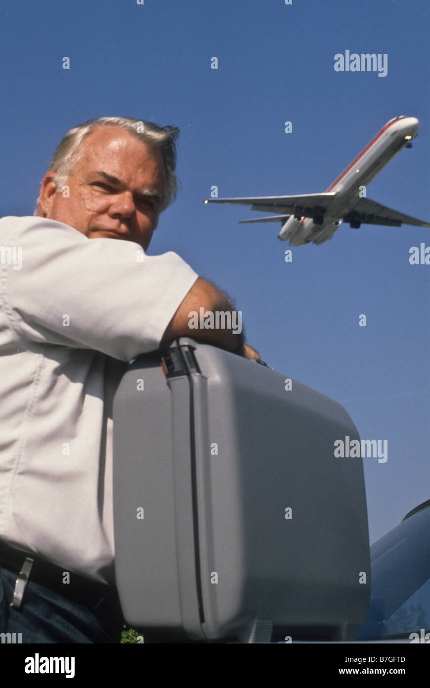 Ältere Mann lehnt sich auf Koffer als Jet fliegen overhead Stockfoto