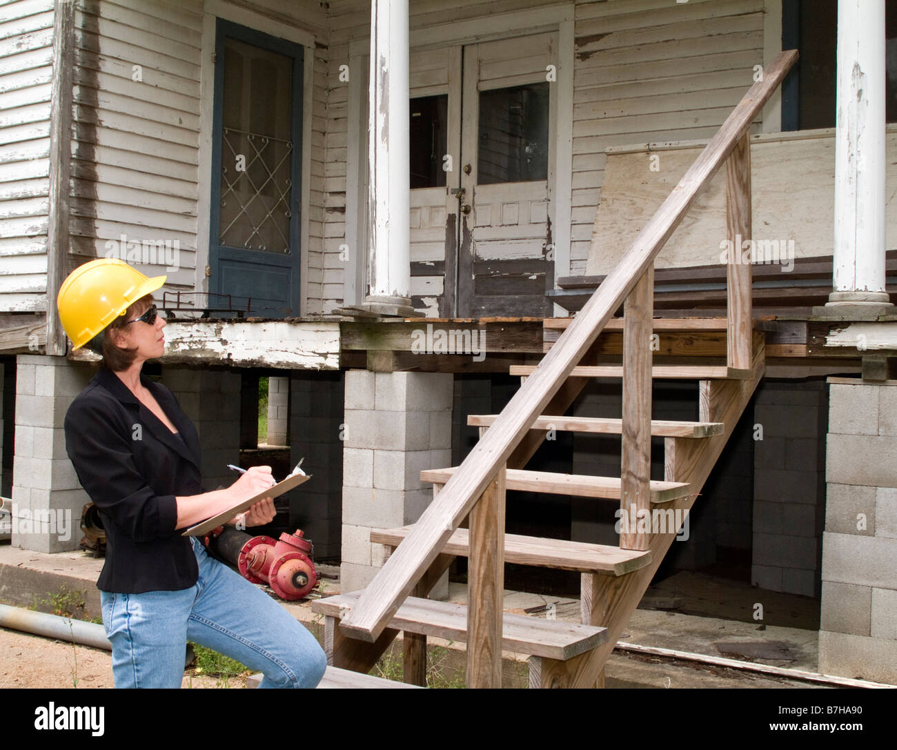 Eine Frau in einen harten Hut hält eine Zwischenablage stehen vor einem alten Haus Stockfoto