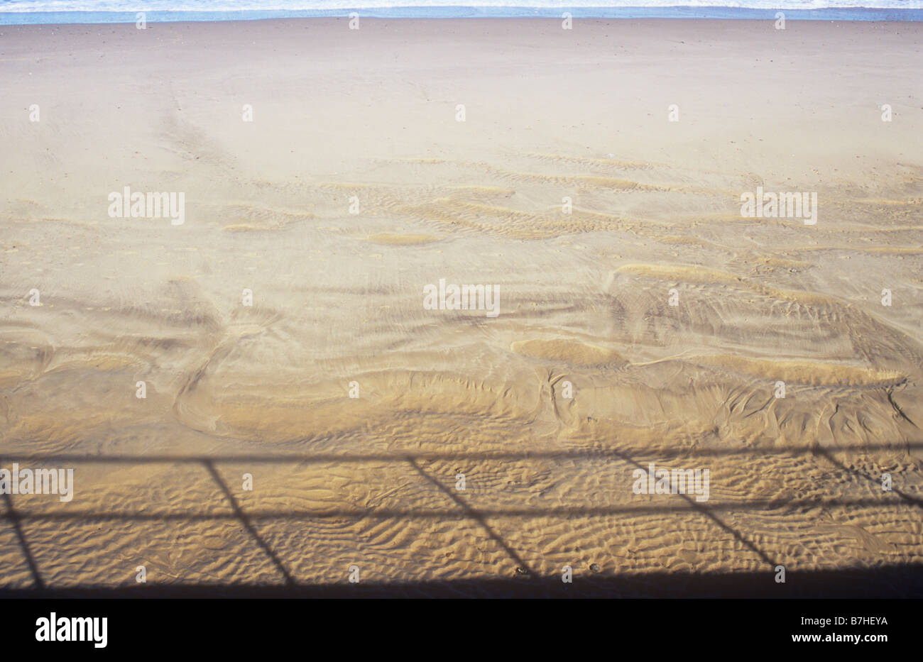 Saubere menschenleeren Sandstrand mit Einschlagkratern getrocknet Gezeiten-Wellen mit entfernten Meer an einem Rand und Schatten von Geländern an anderen Stockfoto