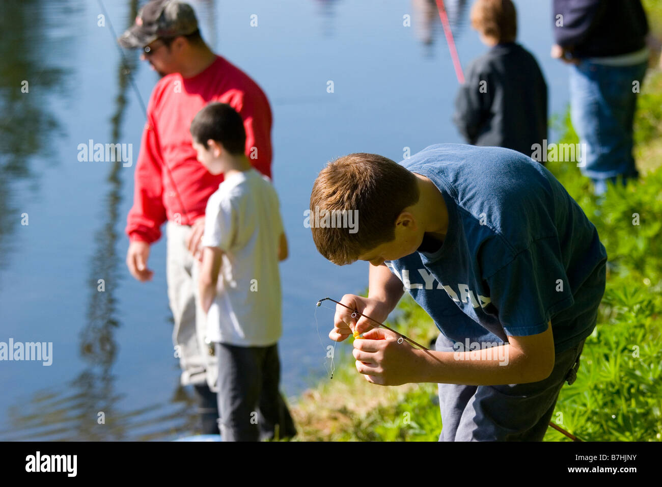 Ein Junge legt Köder auf seinen Haken während des Fischens mit seinem Vater und Bruder Stockfoto