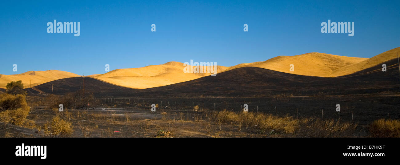 Geschwärzte Hügel kontrastiert orange Hügel und blauer Himmel Stockfoto