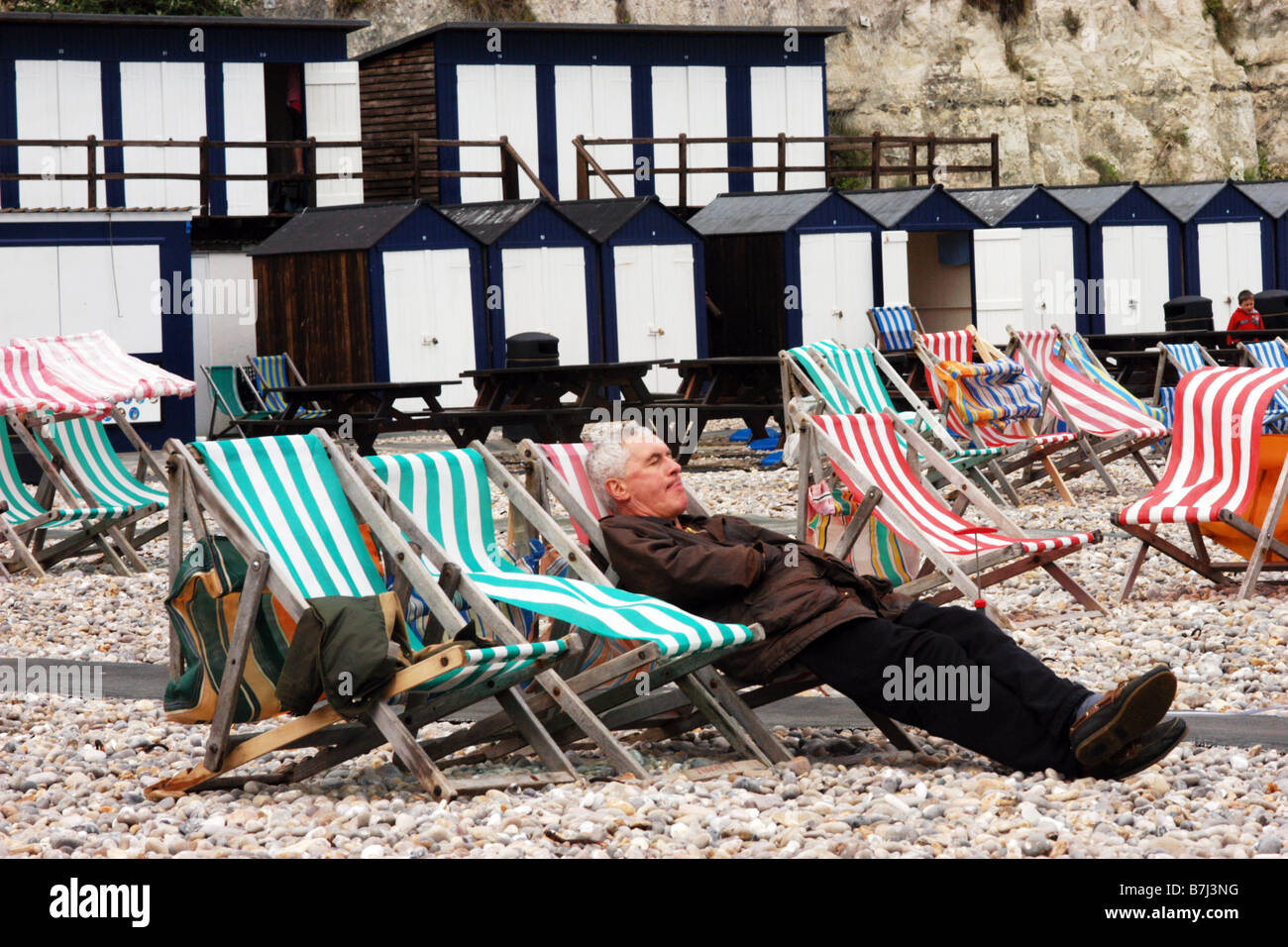 Ein Urlauber sitzt auf einem einsamen kalten Strand auf Liegestühlen, Maifeiertag Bankfeiertag Dorset UK Stockfoto