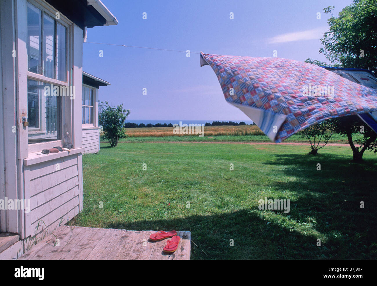 Handgefertigte Steppdecke weht auf der Wäscheleine, Bauernhaus und Meer sichtbar, PEI Stockfoto