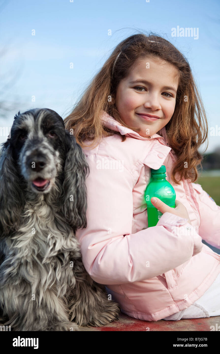 Kaukasische Mädchen und ihr Hund im Park im Winter halten eine Limo-Flasche Stockfoto