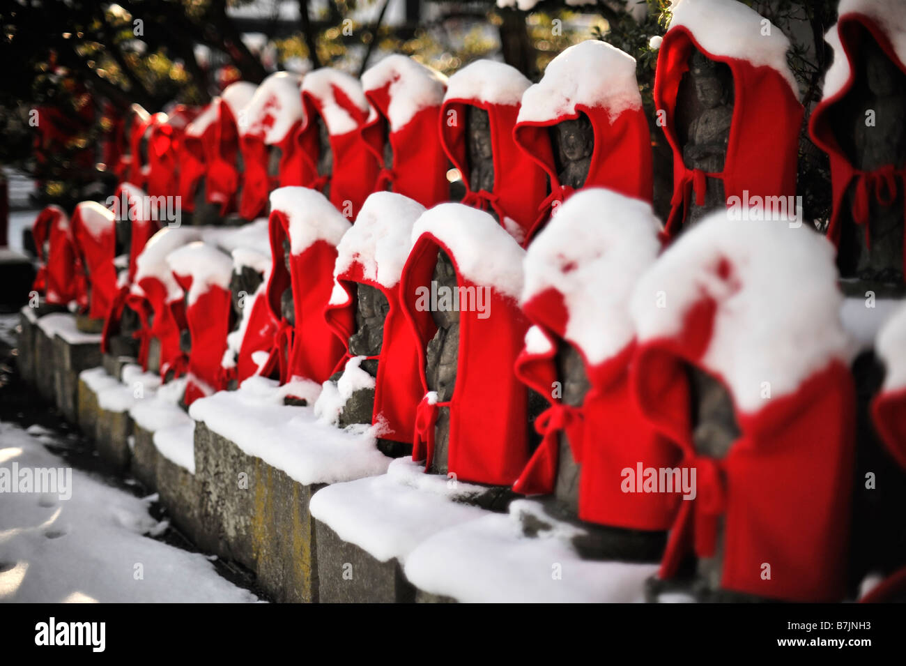 Zwei Reihen von Jizo Statuen tragen rote Umhänge mit Schnee bedeckt. Stockfoto