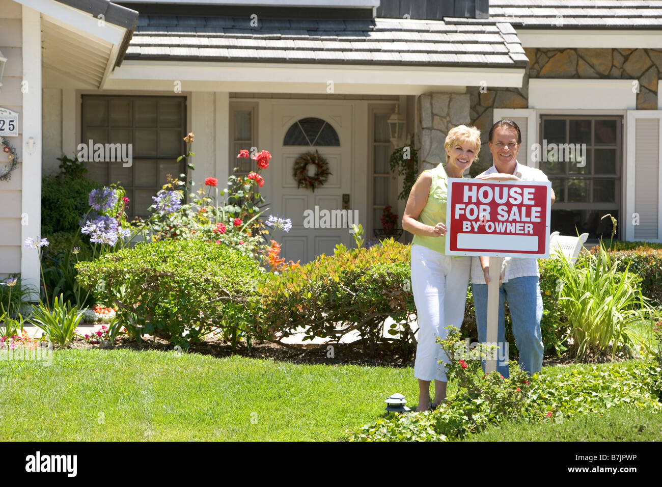 Couple Standing außerhalb Haus mit Schild von Immobilienmakler Stockfoto