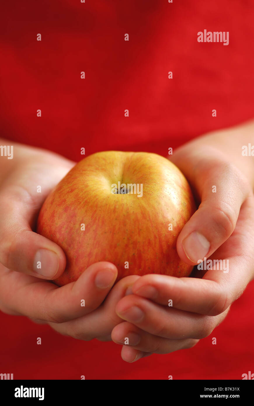 Kind s Hände halten einen Apfel auf rotem Grund Stockfoto