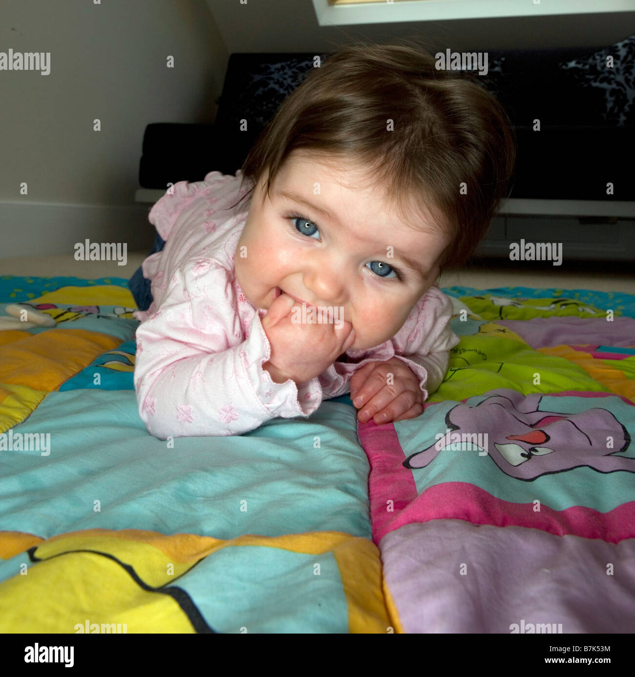 Ein sechs Monate altes Babymädchen kaut auf ihrer Hand, während versuchend, zu kriechen. Stockfoto