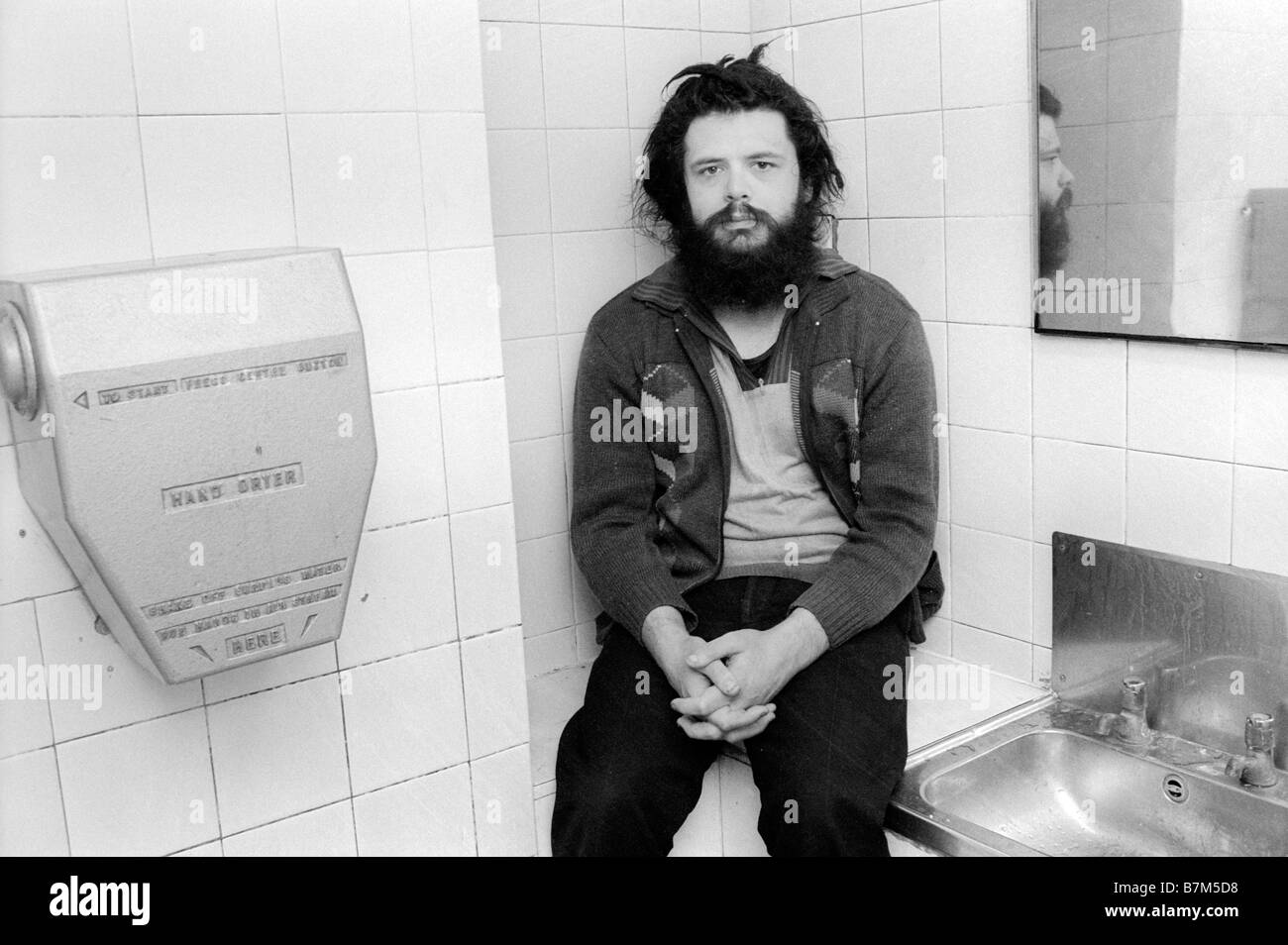 Obdachlosen jungen Mann mit Bart und verfilzte Haare verbringen die Nacht in einer öffentlichen Toilette im Winter Königreich warm zu halten Stockfoto