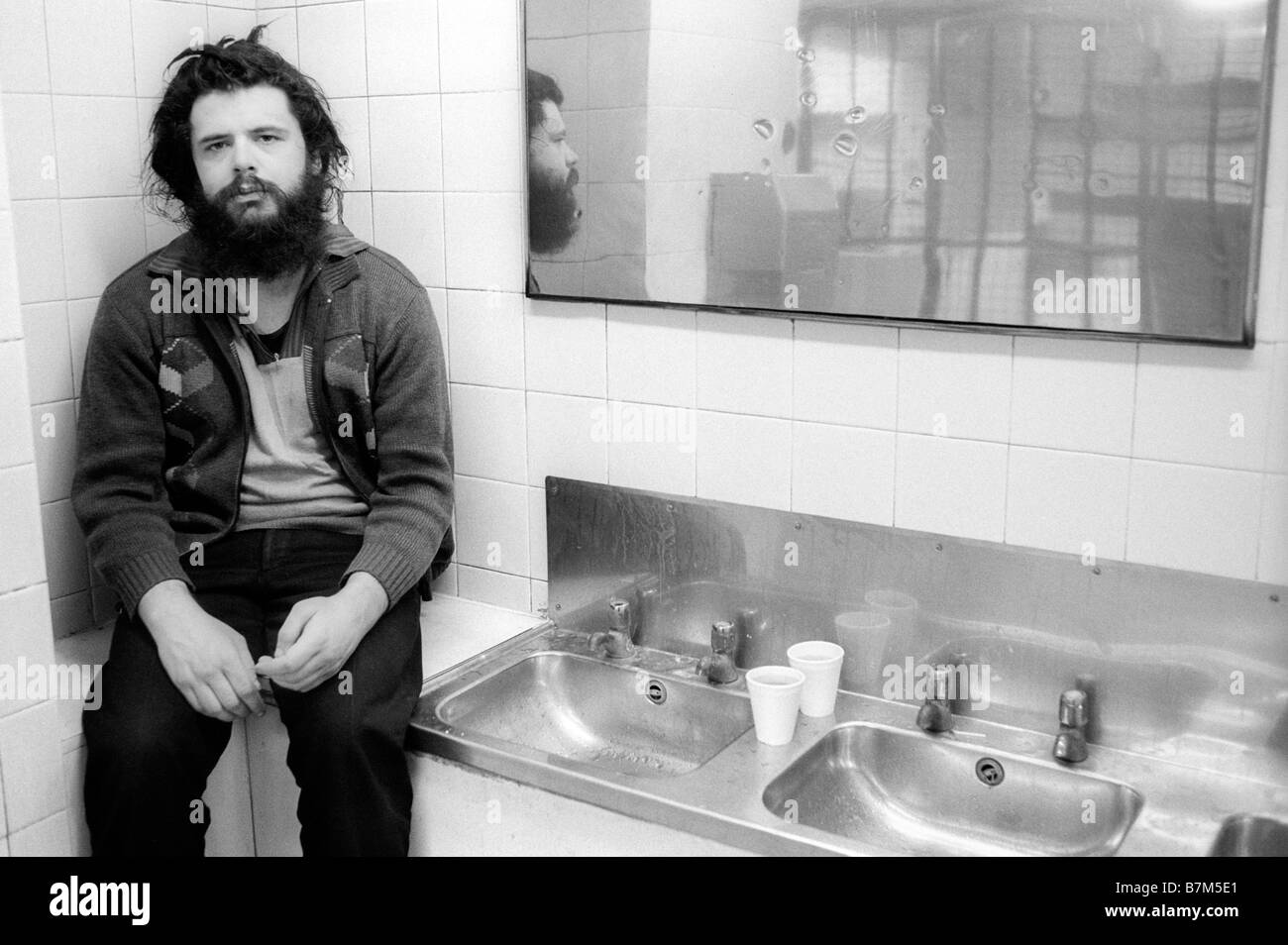 Obdachlosen jungen Mann mit Bart und verfilzte Haare verbringen die Nacht in einer öffentlichen Toilette im Winter Königreich warm zu halten Stockfoto