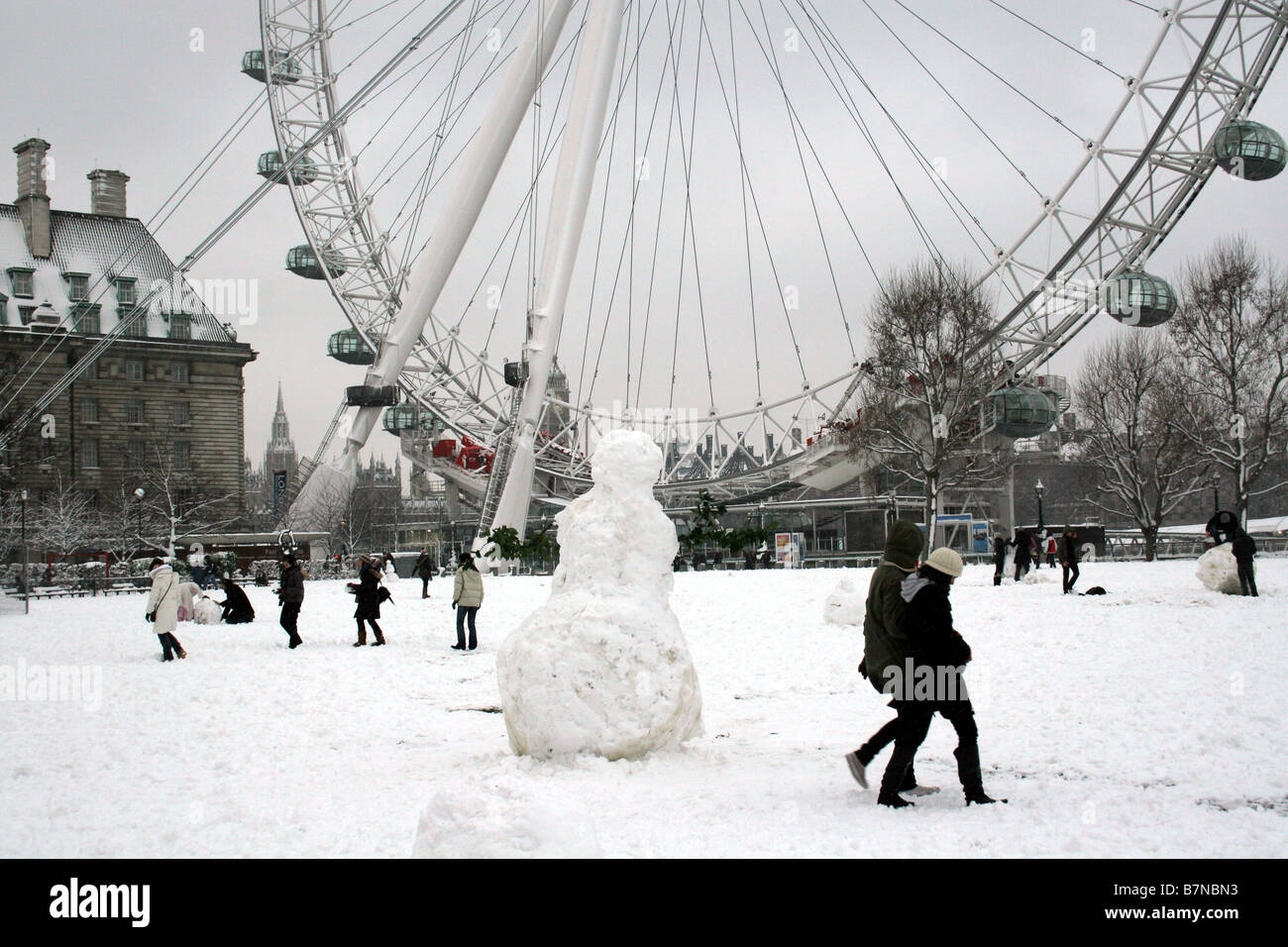 Kinder spielen im Schnee vor dem London Eye, während ein Schneemann Stockfoto