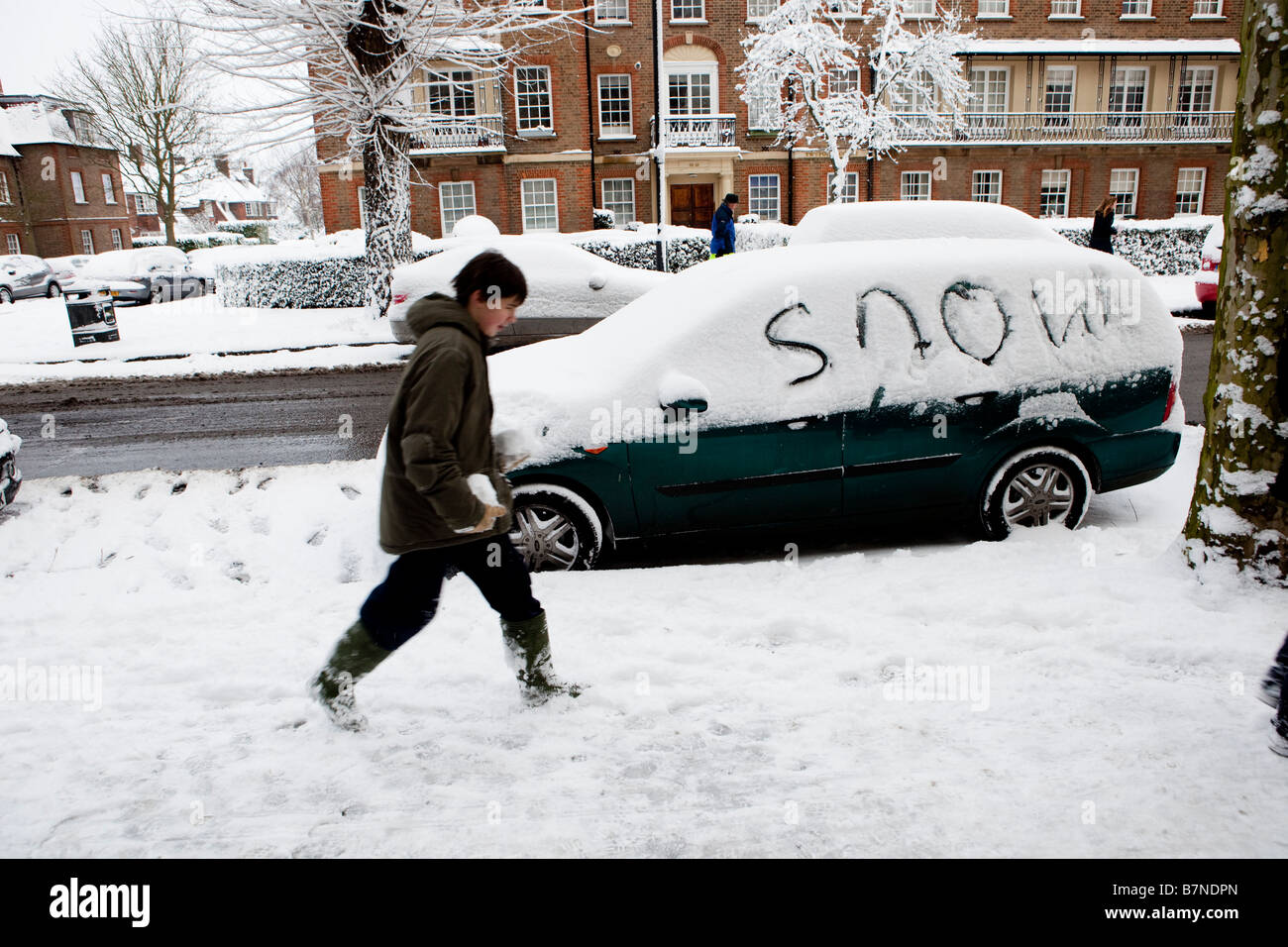 Ein Teenager geht vorbei an einem Auto wo jemand das Wort Schnee in den Schnee geschrieben hat Stockfoto