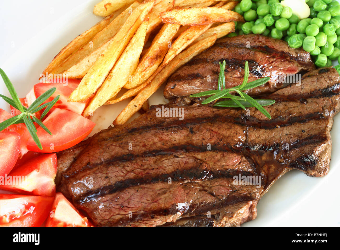 Ein traditionelle Steak Grill mit Rumpsteak französische gebratene Kartoffelchips Tomaten und Erbsen, garniert mit einem Rosmarinzweig Stockfoto