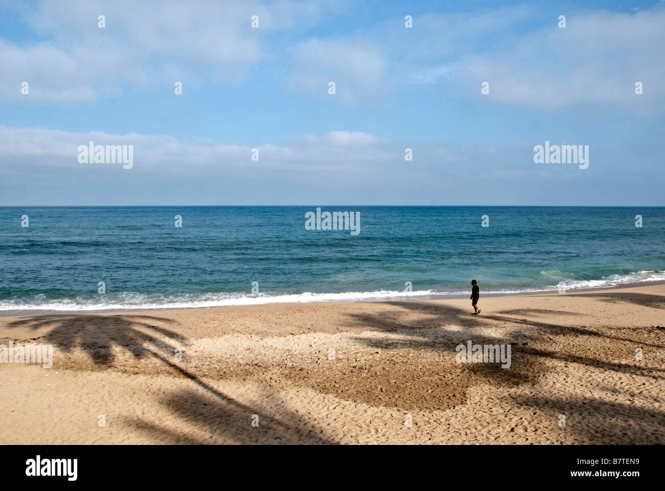 Morgen Strand mit Palmen Baum Schatten und ein einsamer Mann zu Fuß vor dem Hintergrund der azurblaue Meer & Himmel, Sayulita, Nayarit, Mexiko Stockfoto