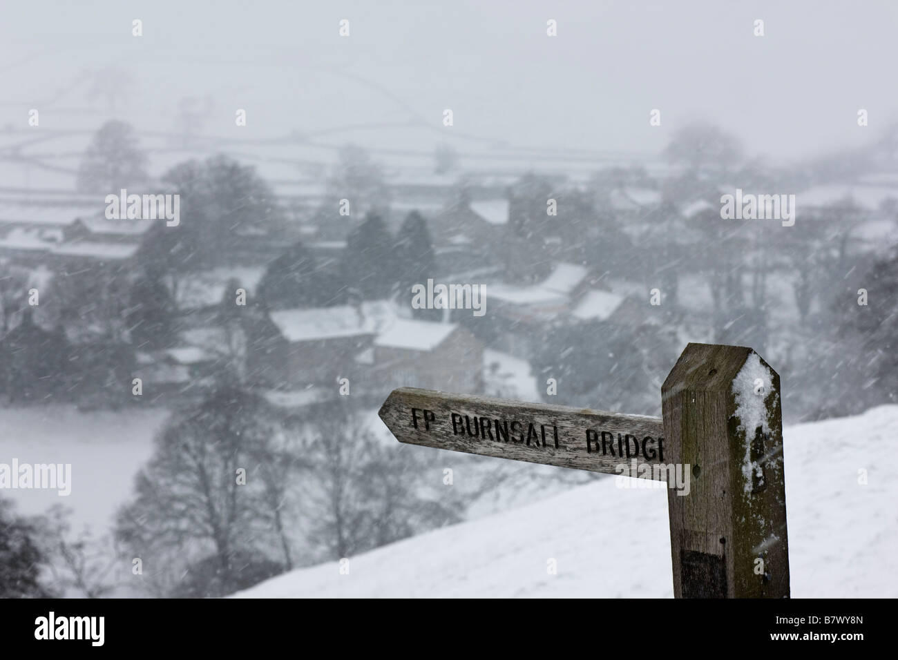 Wegweiser über ein Schnee bedeckt Burnsall Dorf, Yorkshire Dales UK Stockfoto