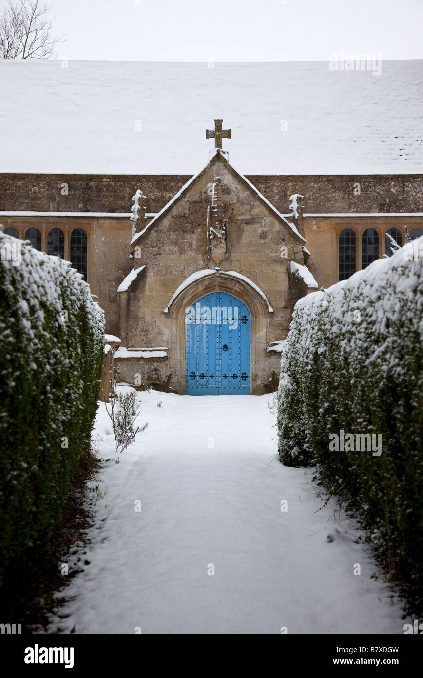 Hell blau hölzerne Eingangstür zum UK Dorfkirche. Pfad im Schnee umgeben von Hecken bedeckt. Stockfoto