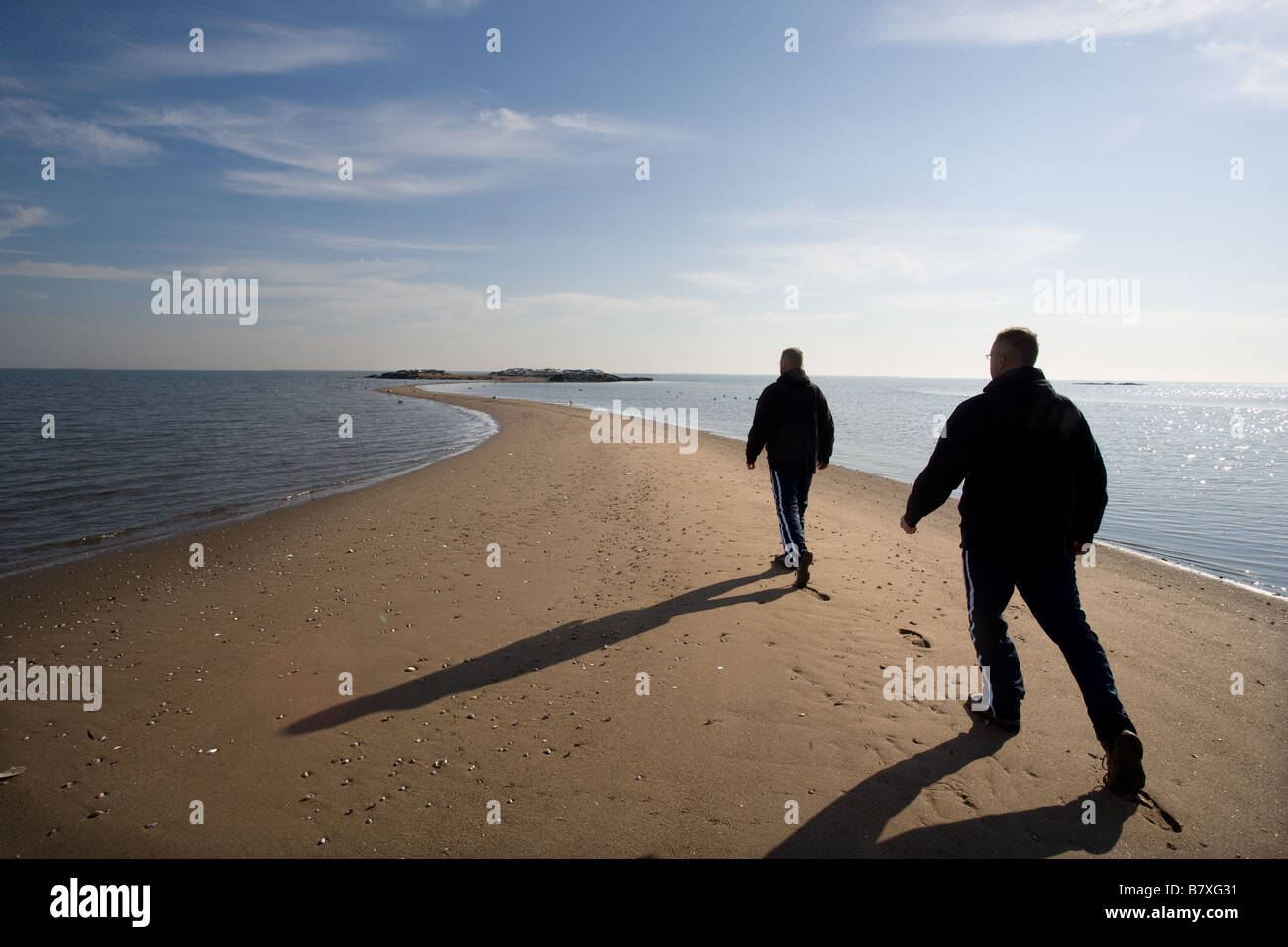 Eine Doppelbelichtung zeigt einen Mann zu Fuß entlang einer Sandbank in Richtung einer Insel mit dem Ozean Stockfoto