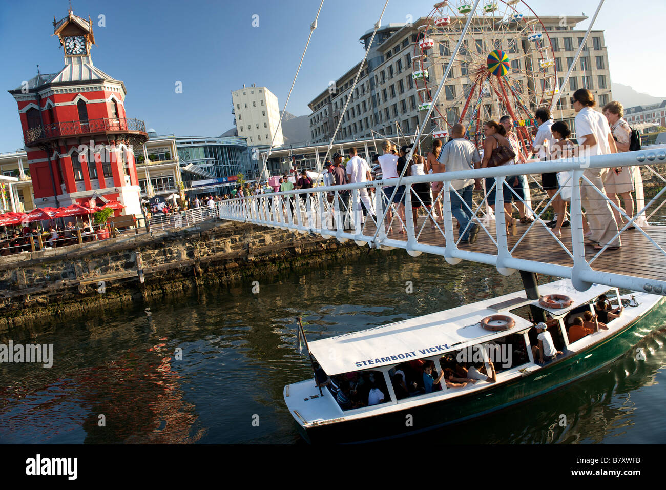 Kleines Boot vorbei unter der Fußgängerbrücke am Clock Tower in Kapstadt Victoria und Alfred Waterfront. Stockfoto