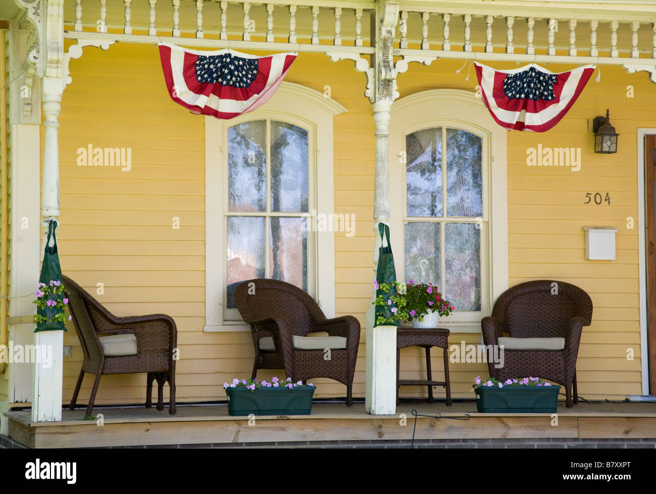 ILLINOIS DeKalb Korbsessel und Blumenkästen auf Veranda des gelben Holzhaus patriotische amerikanische Flagge Banner Stockfoto