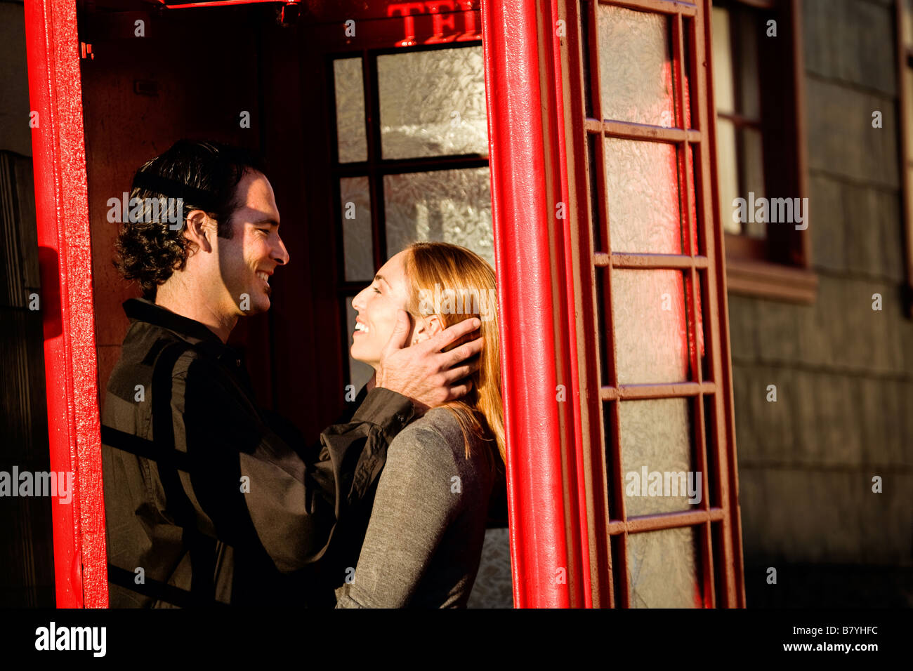 Ein romantisches Paar umarmt und lächelt sich in einer roten Telefonzelle an. Stockfoto