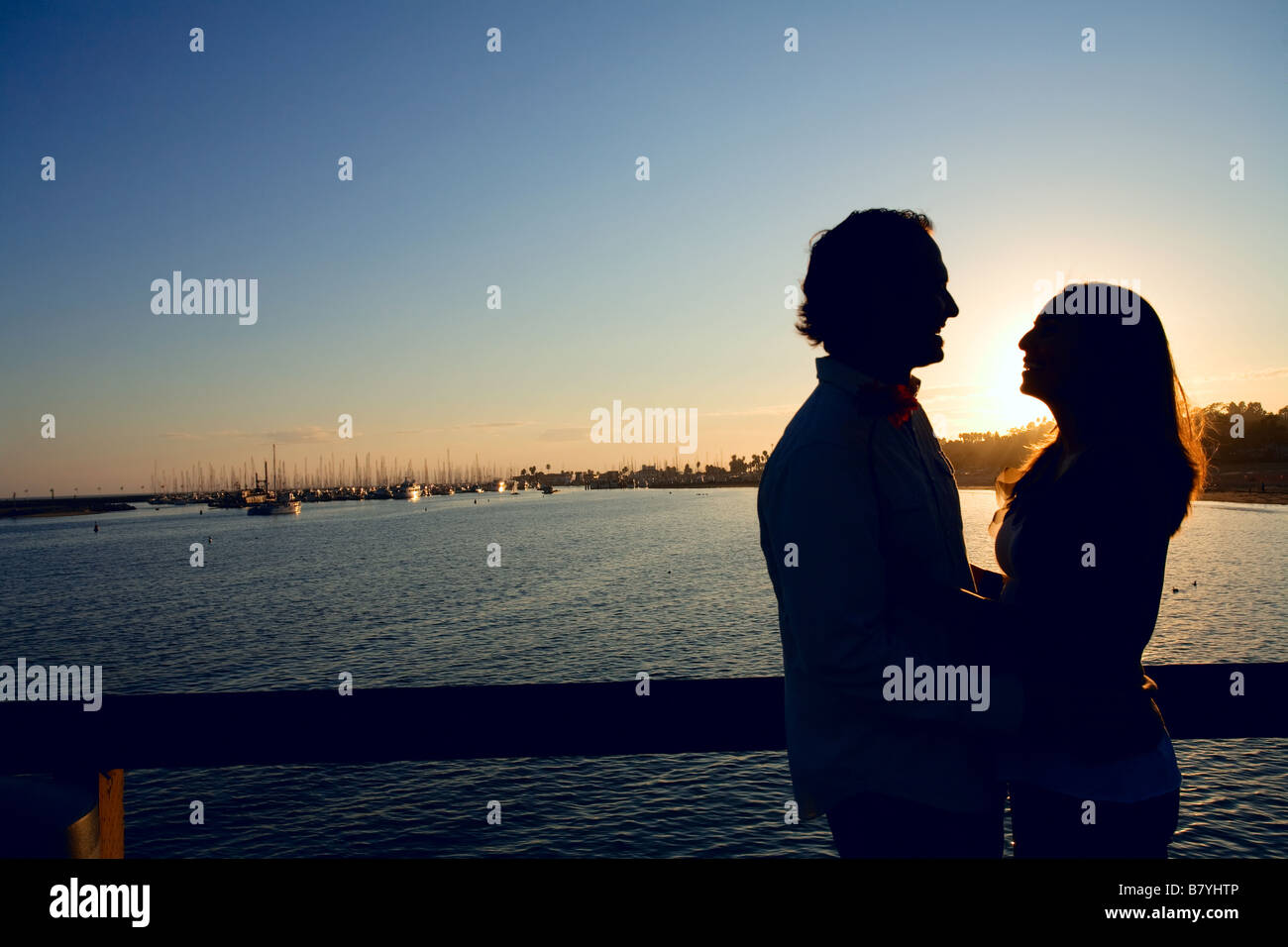 Eine Silhouette eines romantischen Paares bei Sonnenuntergang vor einem Hafen am Meer. Stockfoto