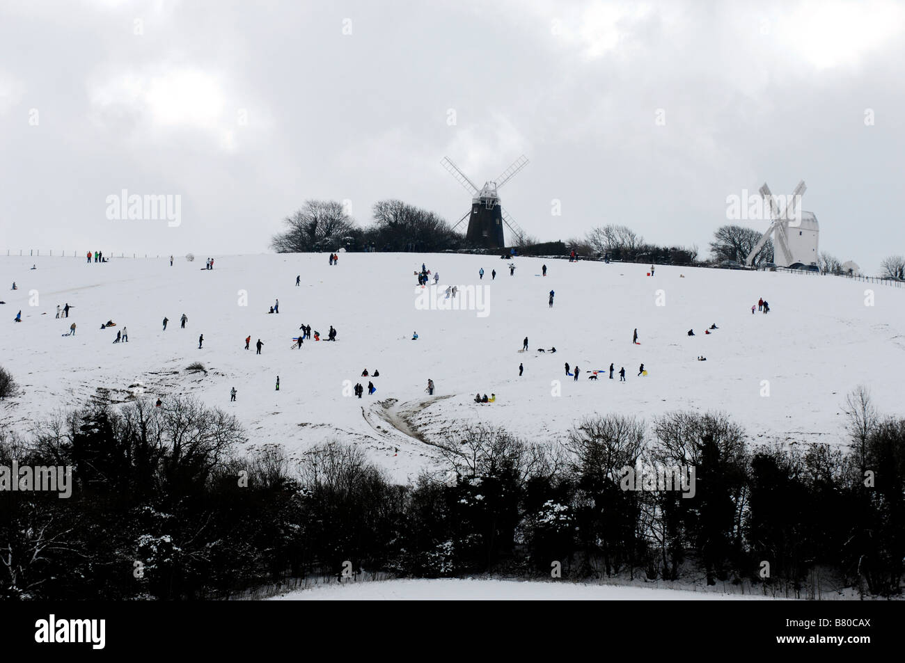 Figuren säumen den Hang wie ein Lowry Malerei, wie sie den Schnee an der Buchse genießen und Jill in Clayton Sussex UK Windmühlen Stockfoto