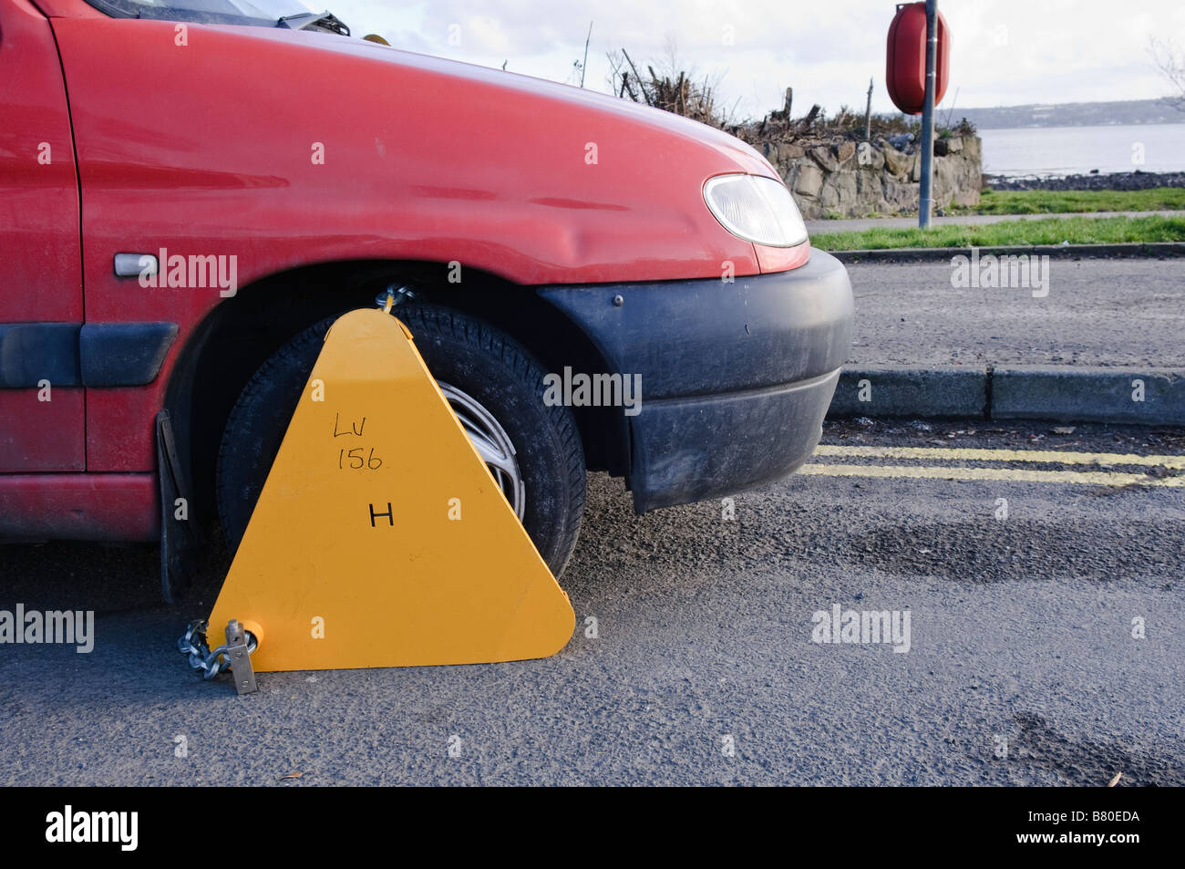 Gelbe Parkplätze/Rad-Klemme auf dem Vorderrad eines roten Autos parkten auf Doppel-gelbe Linien. Stockfoto