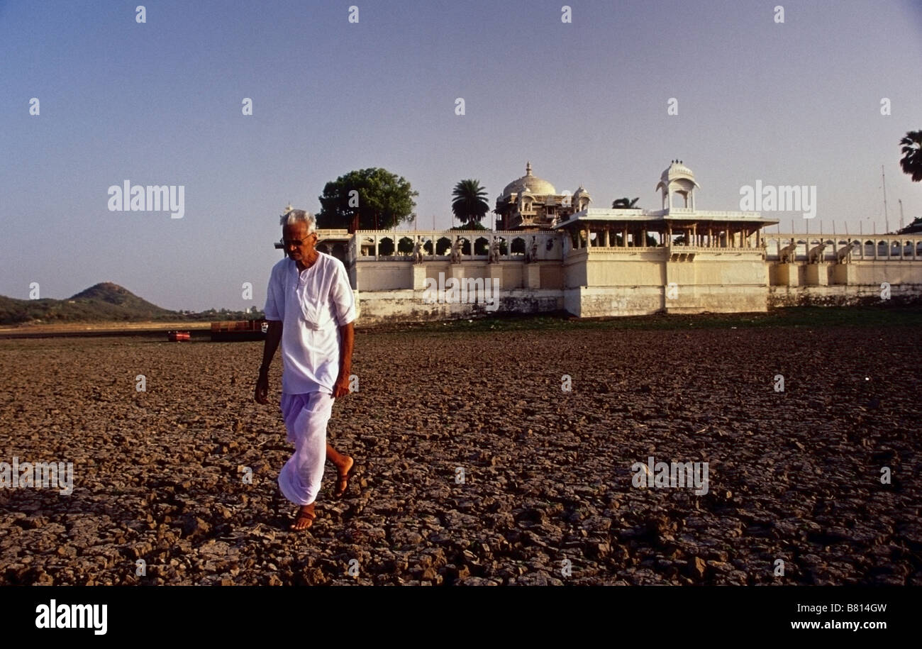 Ein Mann zu Fuß auf den ausgetrockneten See Pichola in Udaipur, Rajasthan, Indien. Jagmandir Palast im Hintergrund Stockfoto