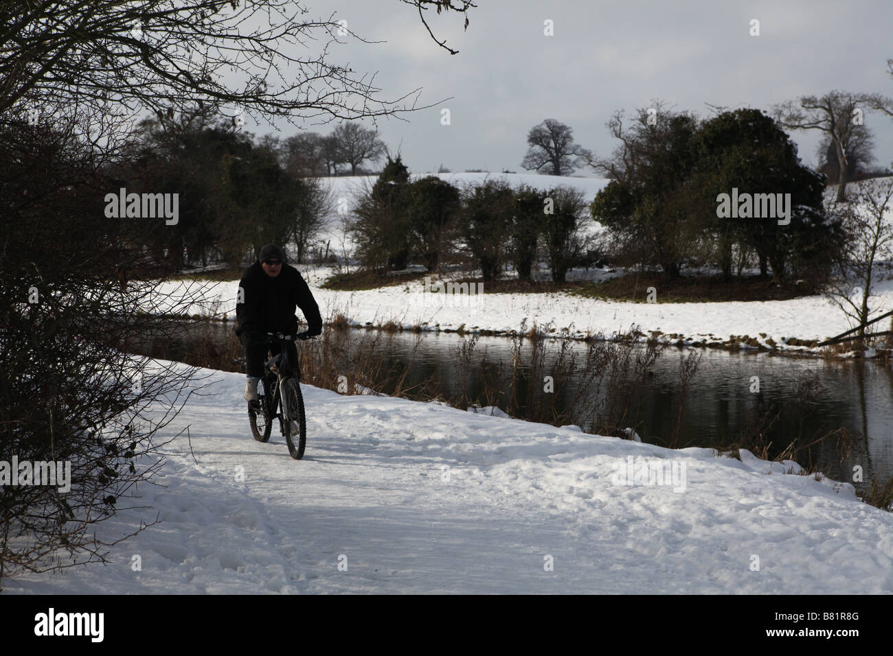 ein Fahrrad Fahrer trotzen Einfrieren Bedingungen und reitet auf seinem Fahrrad durch einen gefrorenen Tal in Hertfordshire mit einem Kanal zu seiner linken Stockfoto