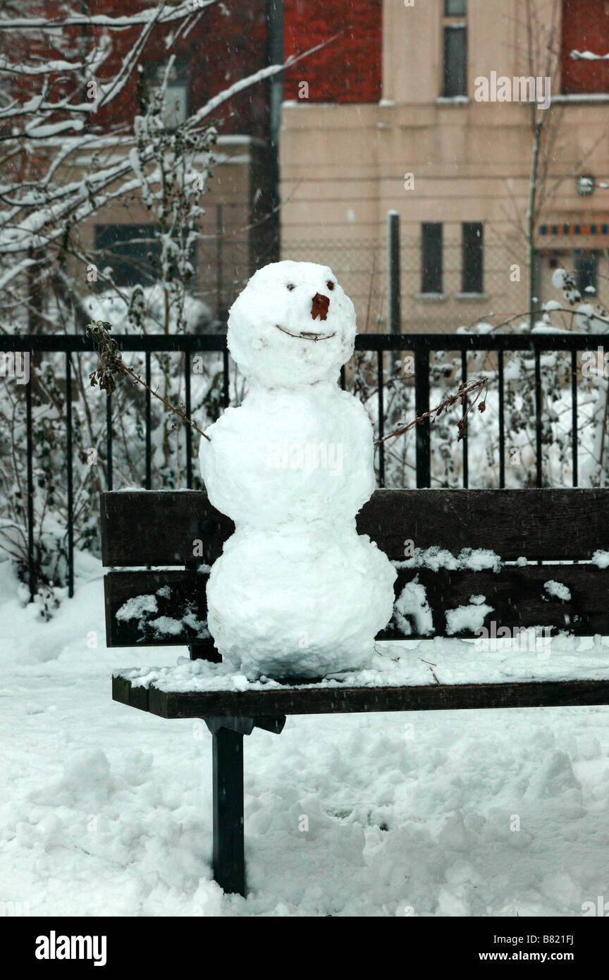 Schnee-Mann sitzt auf einer Parkbank in Ladywell Fields, direkt vor der Lewisham University Hospital Stockfoto