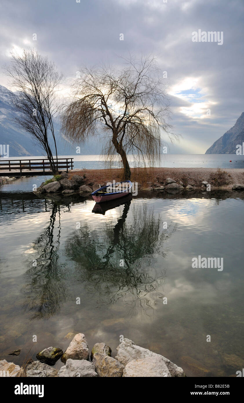 Bäume und Boot spiegeln sich im klaren Wasser des Lago di Garda, Italien Stockfoto