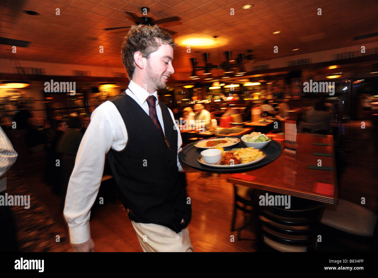 Ein Kellner eilt mit einem Tablett mit Essen in einem gut besuchten Restaurant Bradford, West Yorkshire Stockfoto