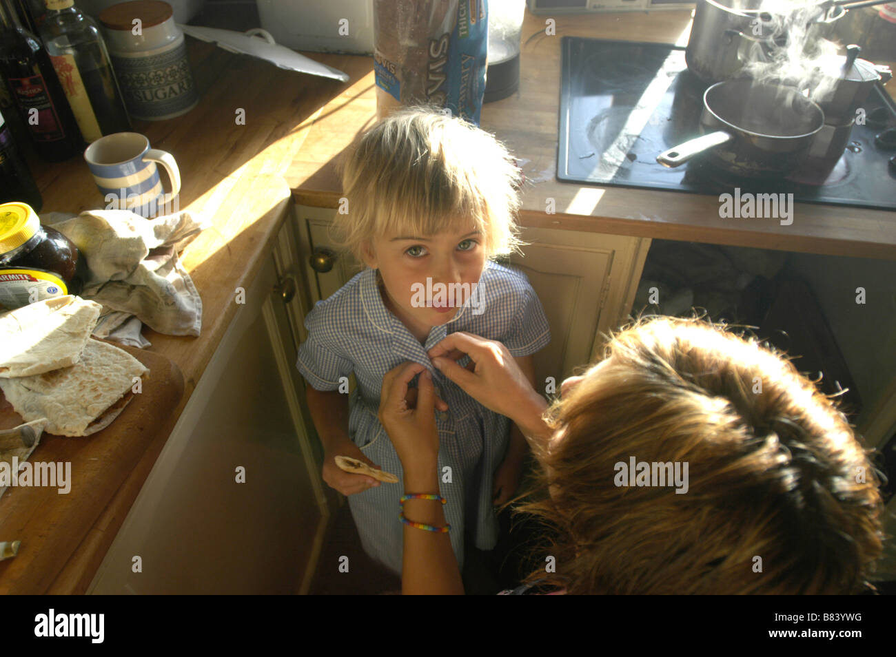 Ein 5 Jahre altes Mädchen Kleid für Schule in das Chaos der Frühstück geholfen. Stockfoto