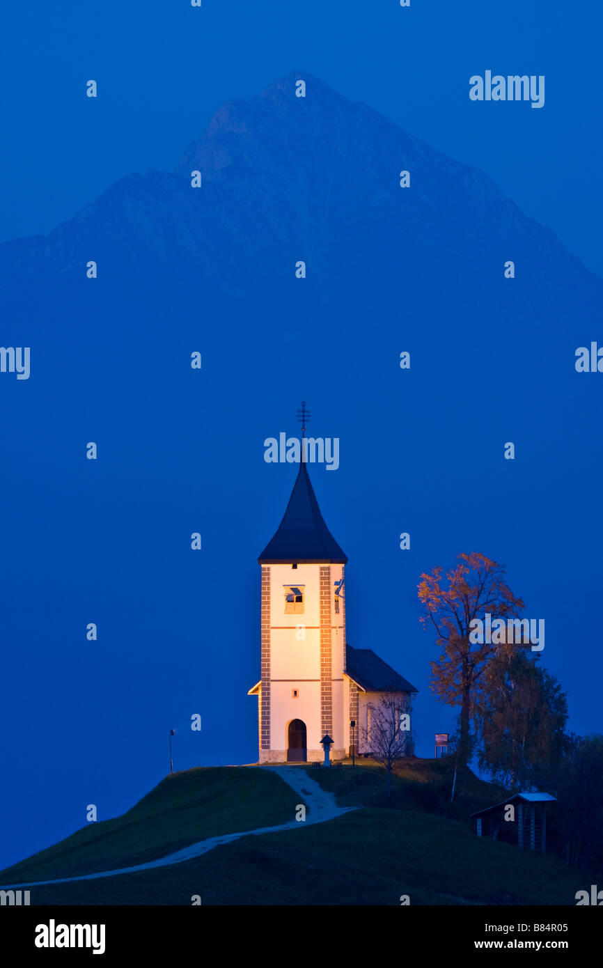 Primoz Kirche mit Storzic in Kamnik-Savinja Alpen Berg hinter Blaustich zu Kirche Hintergrund beleuchtet Stockfoto