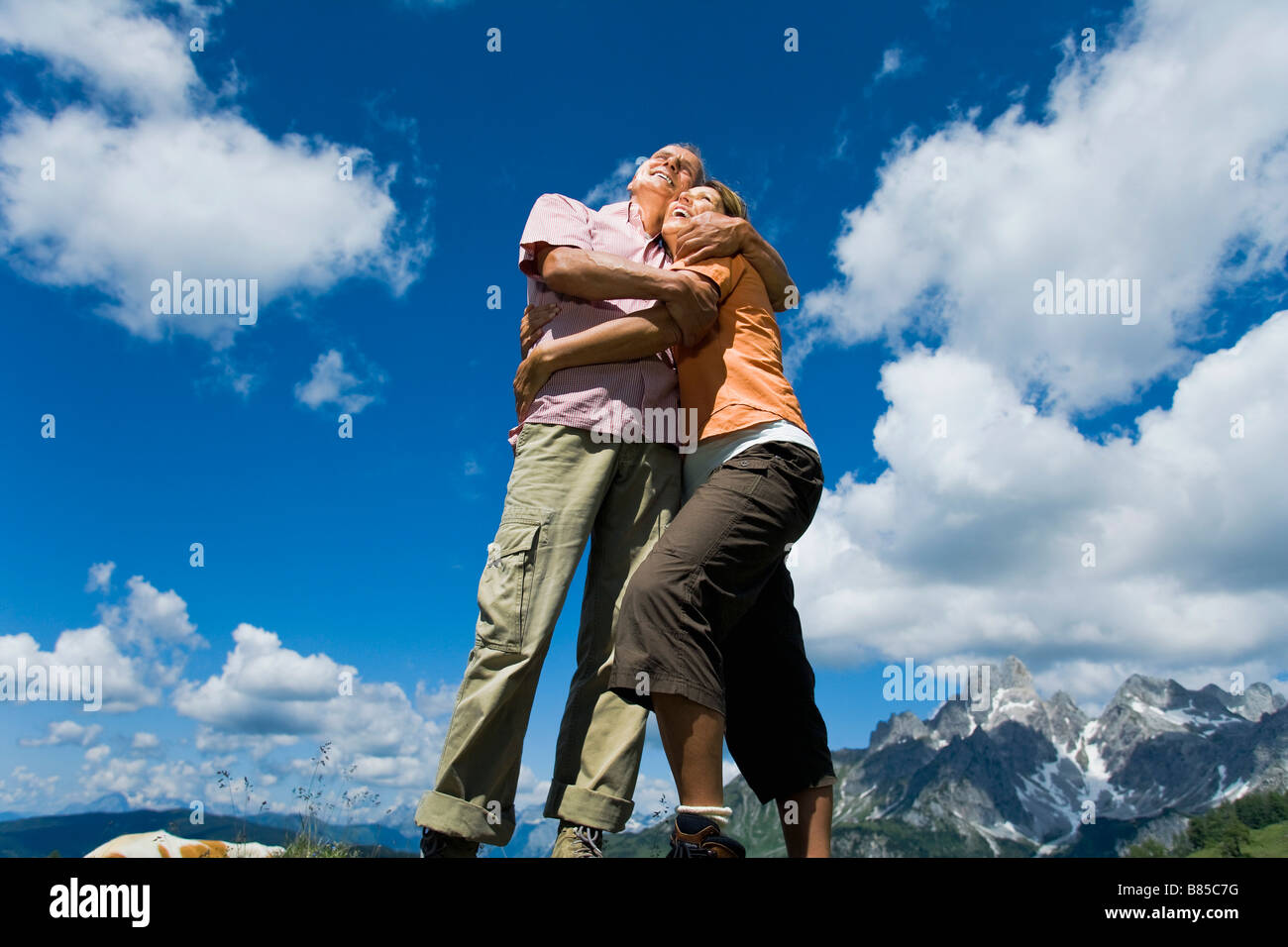 älteres paar stehen auf Felsen in den Bergen, umarmen einander Stockfoto