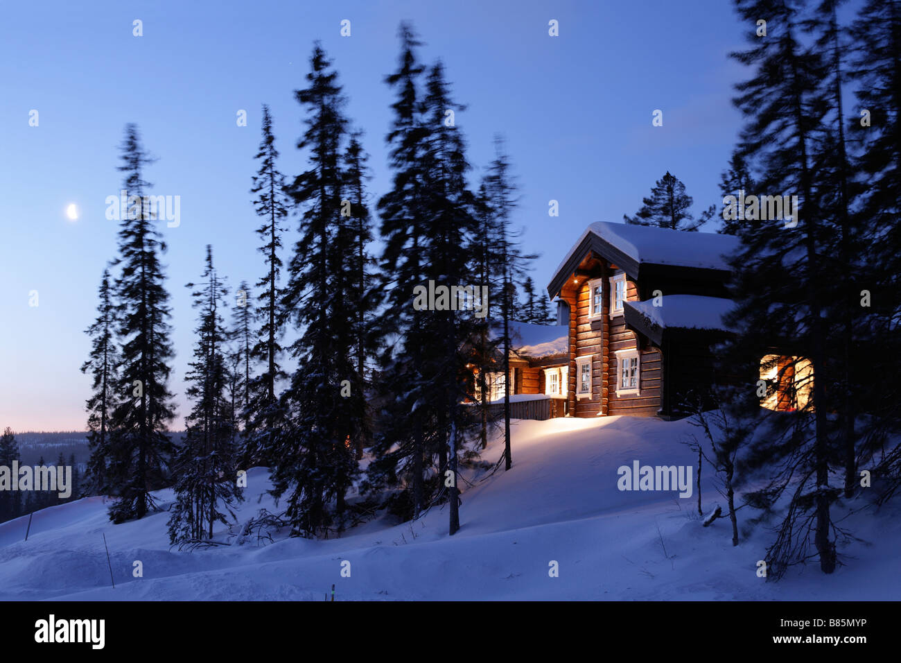 Norwegisches Blockhaus in verschneiter Landschaft. Einbruch der Dunkelheit oder Dämmerung. Stockfoto