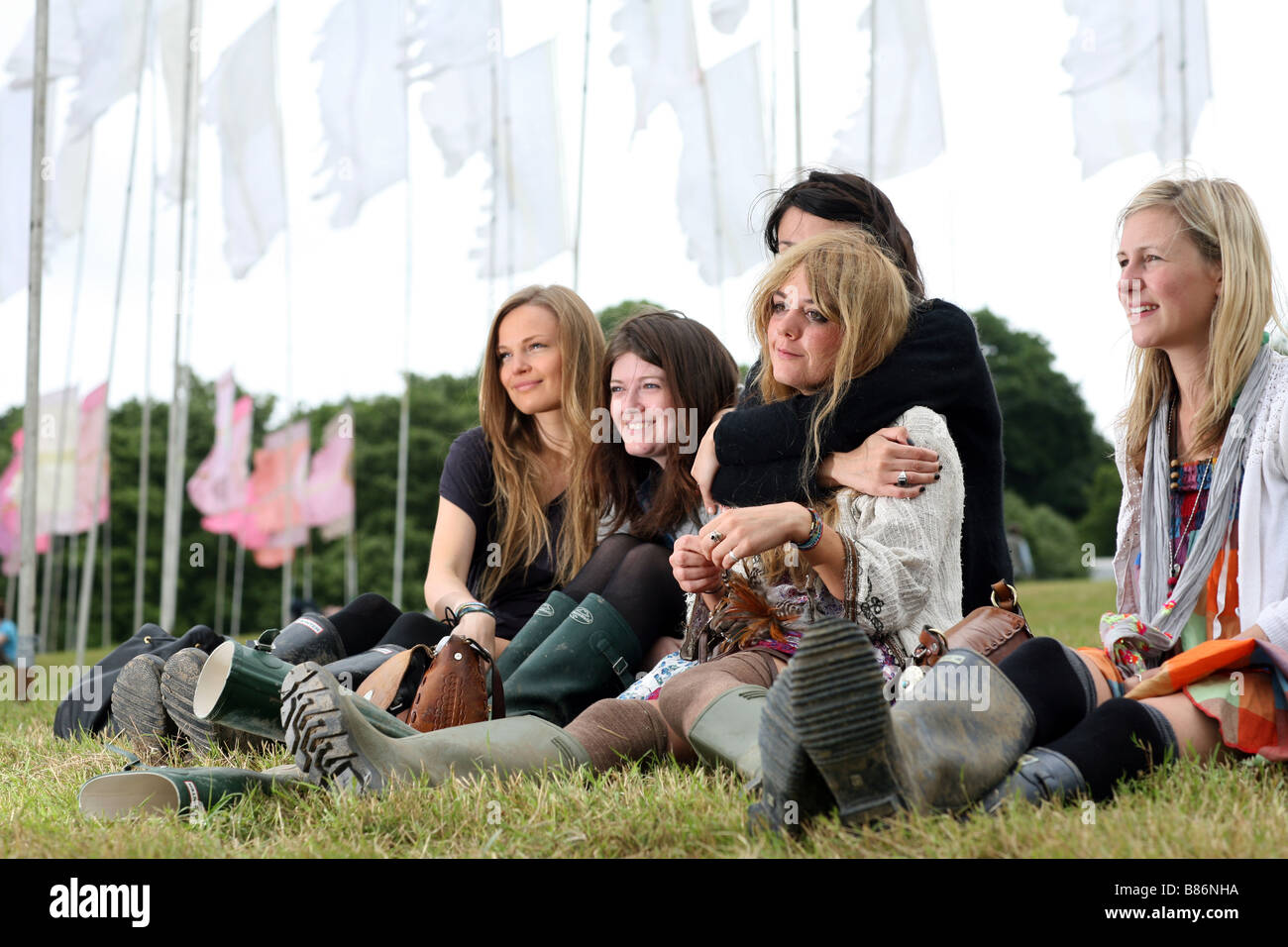 Eine Gruppe von Mädchen genießen Sie die Musik unter Flaggen auf dem Glastonbury Festival in Pilton, Somerset in England saß. Stockfoto