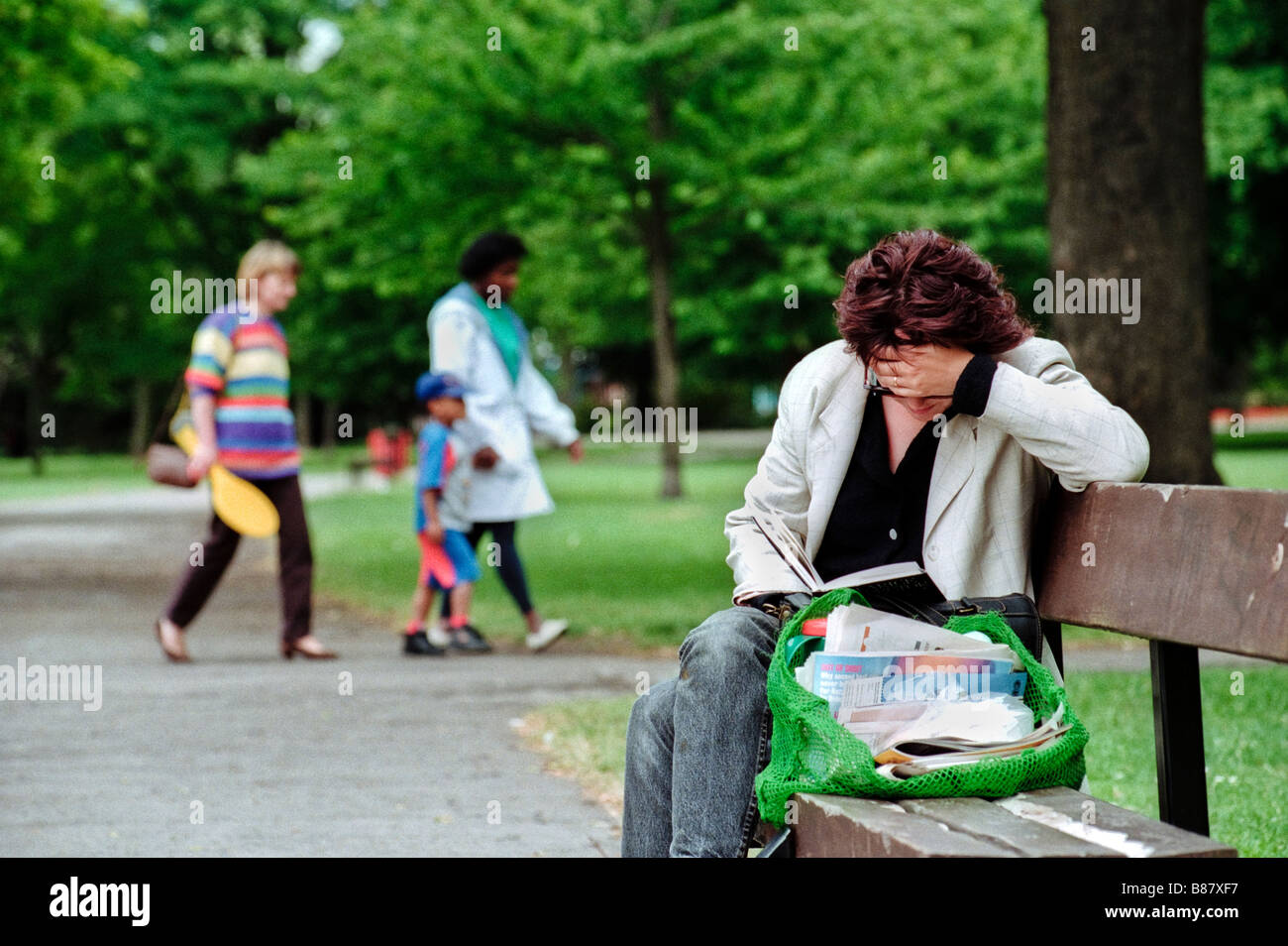 Frau Lesebuch Frau saß auf der Bank und liest Buch Menschen vorbeigehen im Hintergrund im Victoria Park Cardiff South Wales UK Stockfoto