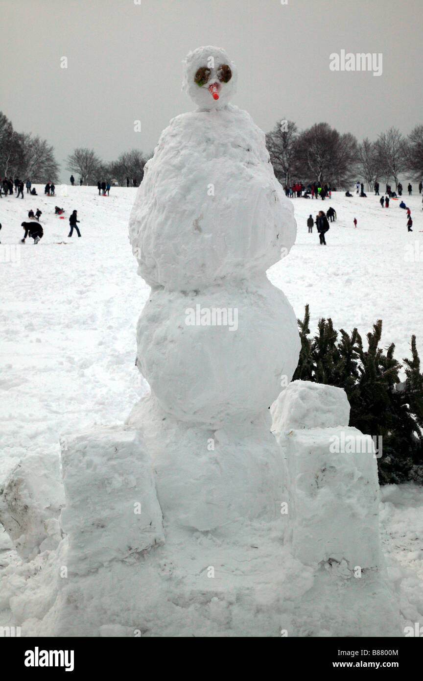 Avantgarde-Schneemann auf Hilly Fields Park, Lewisham mit der lokalen Bevölkerung spielen im Schnee im Hintergrund Stockfoto