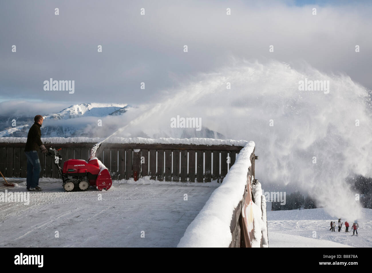 Honda Hybrid-Schneefräse verfolgt auf Holzbalkon in Ski-Restaurant Mann Clearing frischen Pulverschnee Schnee mit Stockfoto